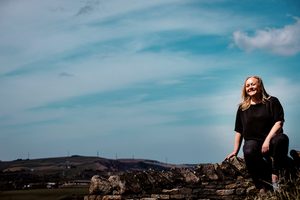 Anna Short sitting on a dry stone wall overlooking the Saddleworth countryside in Oldham, Greater Manchester.
